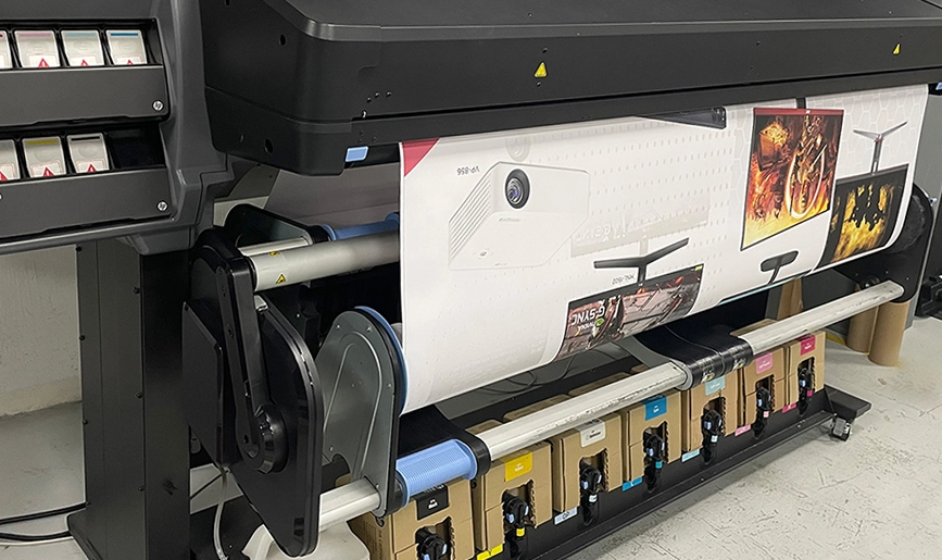 Máquina Plotter HP para la impresión a gran formato, se encuentra imprimiendo una lona con diseño de aparatos electrónicos.